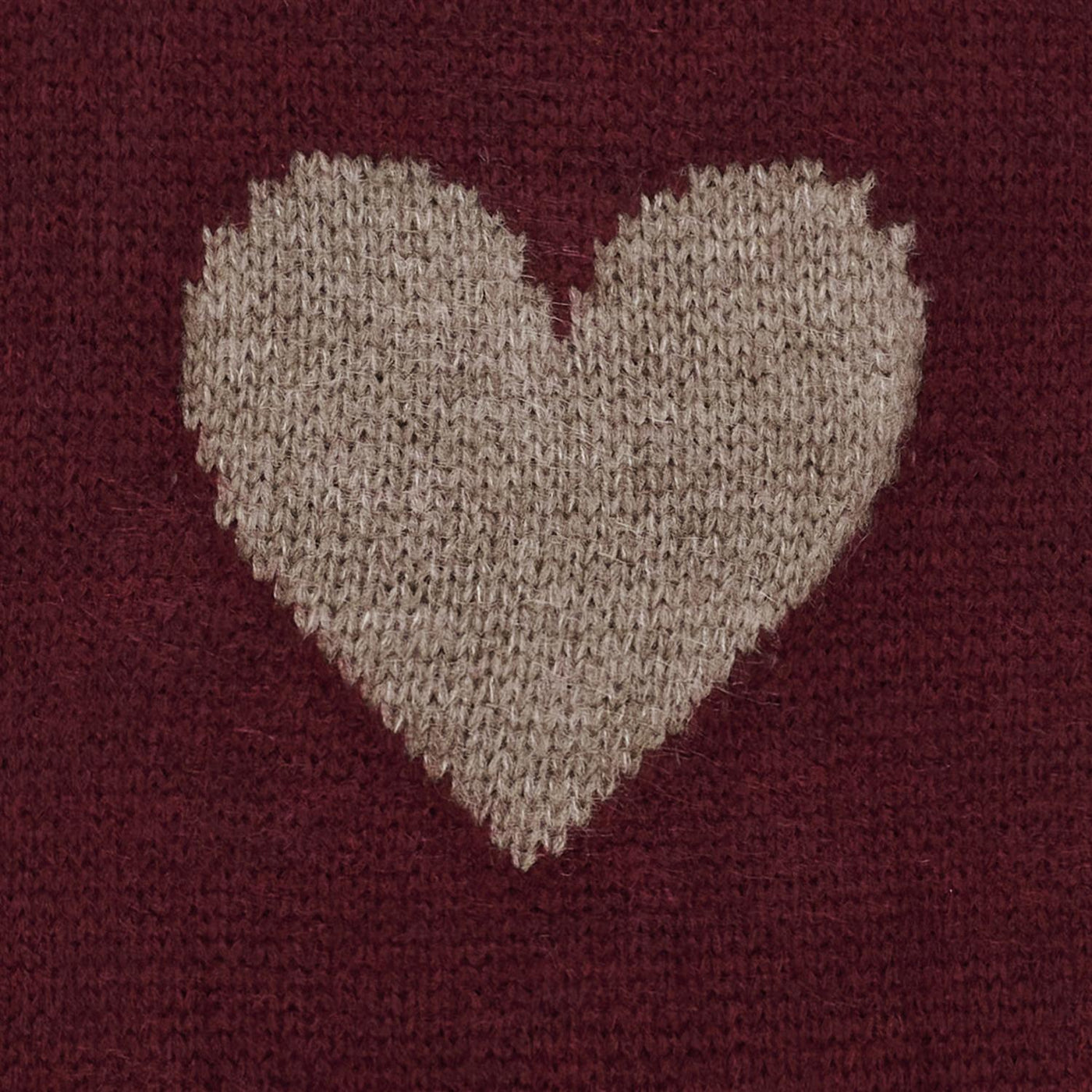 Nærbilde av strikkegenser med beige hjerte-design på rød bakgrunn.