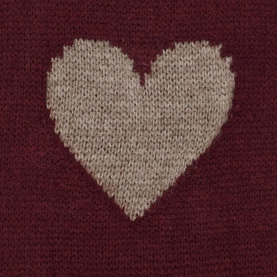 Nærbilde av strikkegenser med beige hjerte-design på rød bakgrunn.