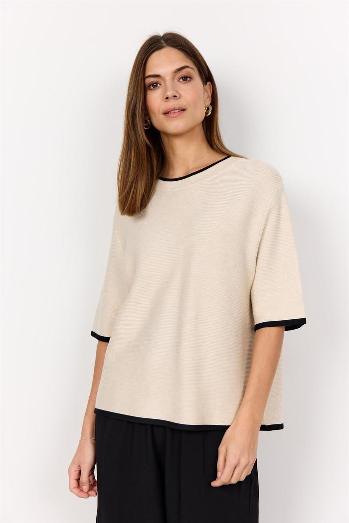 Lys beige t-skjorte med svart kant, rund hals, avslappet passform, vist på modell.