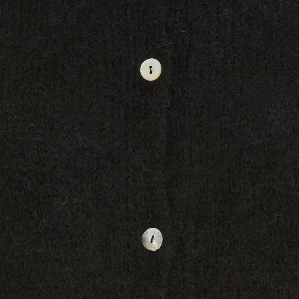 Nærbilde av svart strikket cardigan med lyse knapper på glatt stoff.