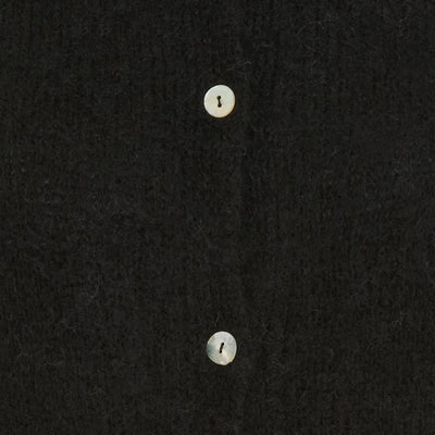 Nærbilde av svart strikket cardigan med lyse knapper på glatt stoff.