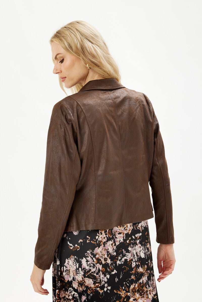 Kvinne sett bakfra med brun jakke med jakkeslag og blomstrete skjørt. Blondt hår.