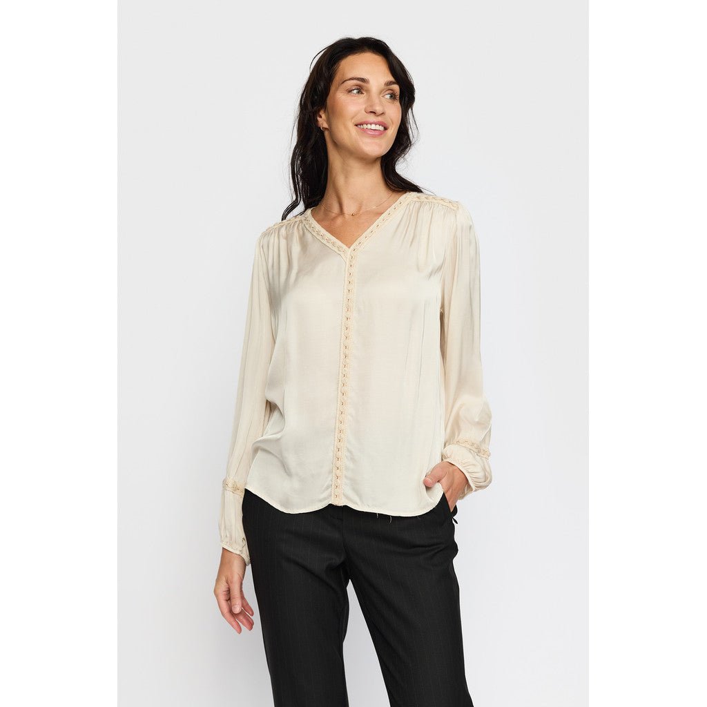 Lys bluse med V-hals og blondedetaljer, plisserte skuldre og elastiske mansjetter.