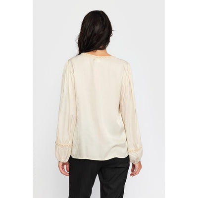 Lys bluse sett bakfra, plisserte skuldre, elastiske mansjetter med blondedetaljer.