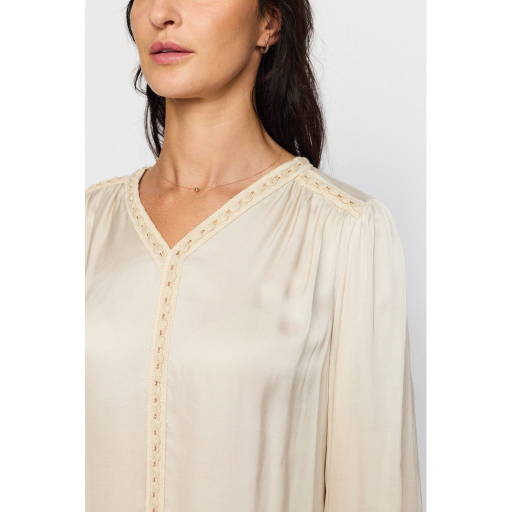 Lys bluse med V-hals og blonder, plisserte skuldre, elastiske mansjetter med blondedetaljer.