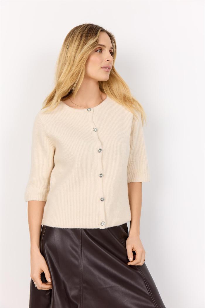 Lys beige cardigan med knapper, trekvart ermer og strikket tekstur. Modellen har langt, blondt hår.