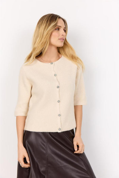 Lys beige cardigan med knapper, trekvart ermer og strikket tekstur. Modellen har langt, blondt hår.