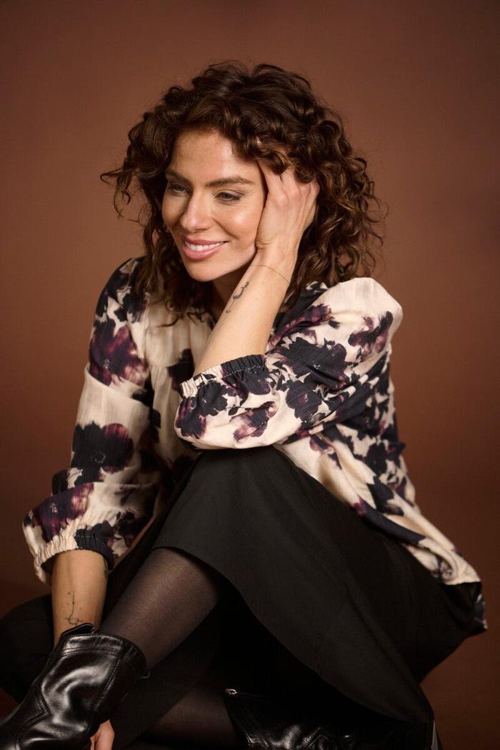 Person med krøllete hår i Bonny Shirt med blomster, lange ermer og V-utringning, smilende.