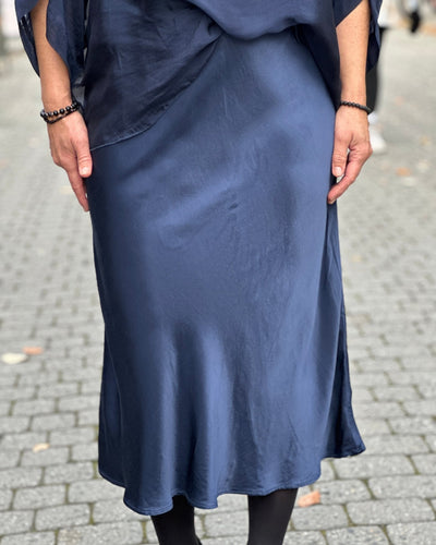 Person iført mørkeblått, skinnende satengskjørt med flytende fall, knelangt eller lengre.