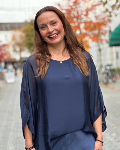 Kvinne i mørkeblå, løstsittende bluse med lagdelt design, smilende utendørs om høsten.