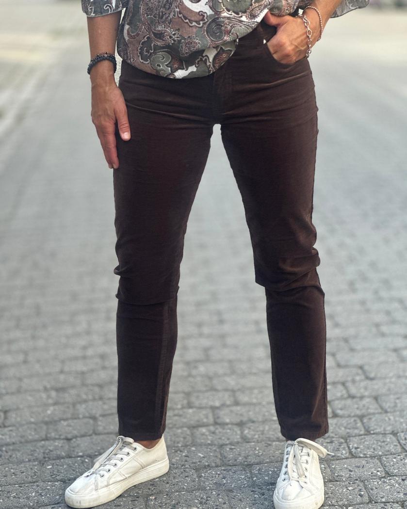 Person i mørkebrune jeans med stram passform og hvite sko, står på brosteinsbelagt vei.