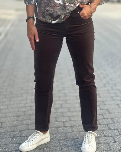Person i mørkebrune jeans med stram passform og hvite sko, står på brosteinsbelagt vei.