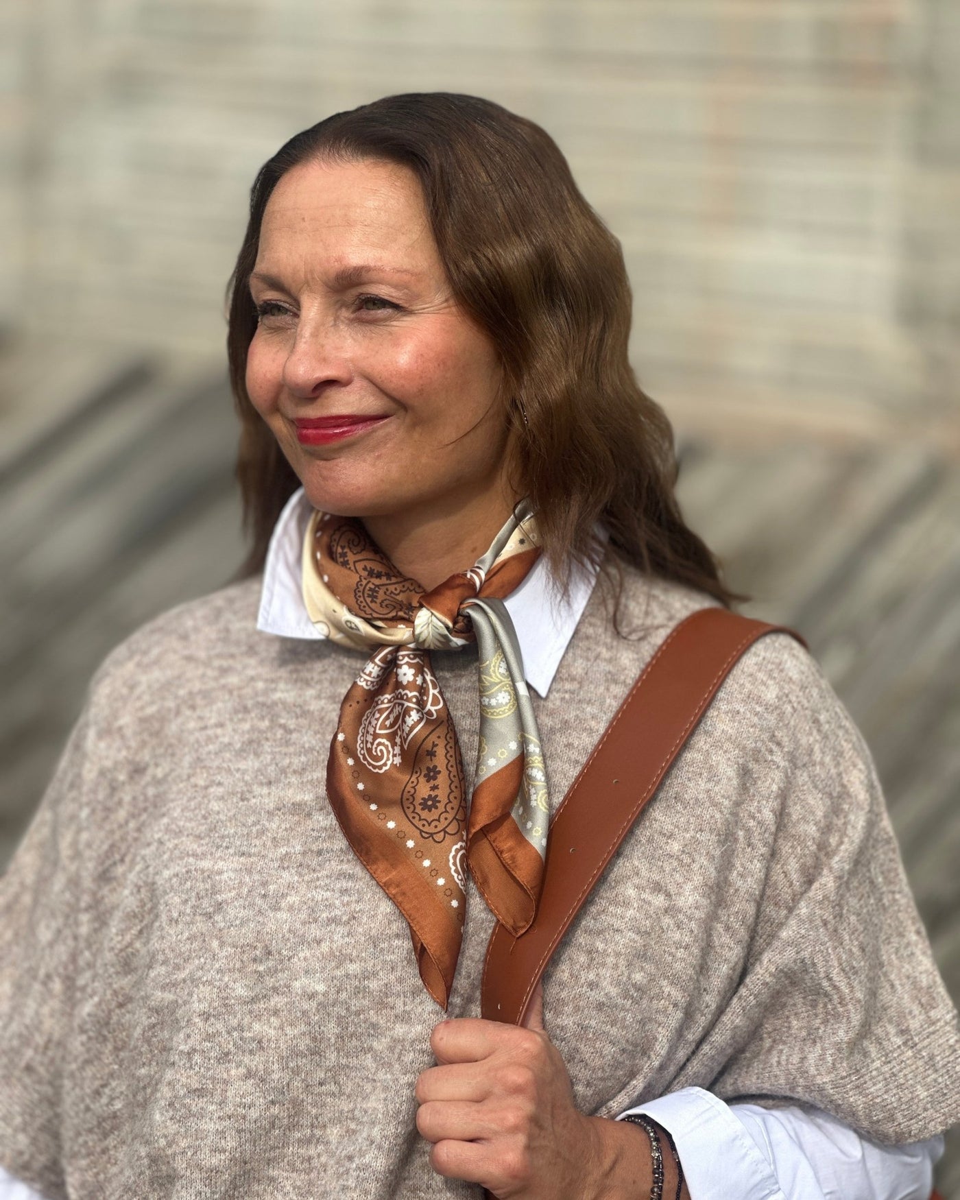 Skjerf med brune, grå og beige paisleymønstre, knyttet rundt halsen på en person.