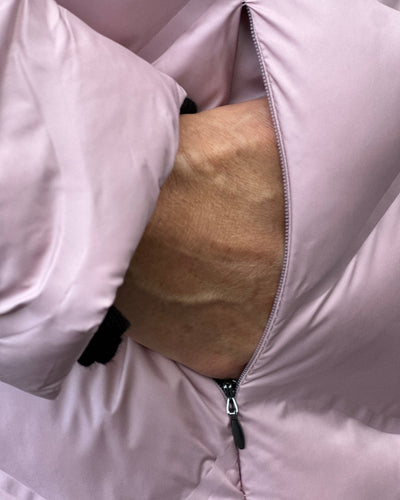 Hånd stikker inn i lomme på rosa quiltet jakke med glidelås.