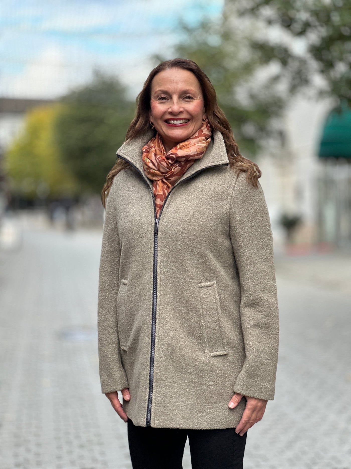 Ullblandet jakke med glidelås, to lommer, høy krage. Bæres av smilende person utendørs.
