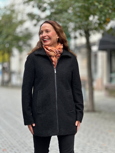 Svart ulljakke med glidelås, enkel stil, bæres av person ute i urbant miljø.