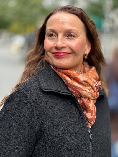 Kvinne med svart jakke med glidelås og oransje skjerf i urbant miljø.