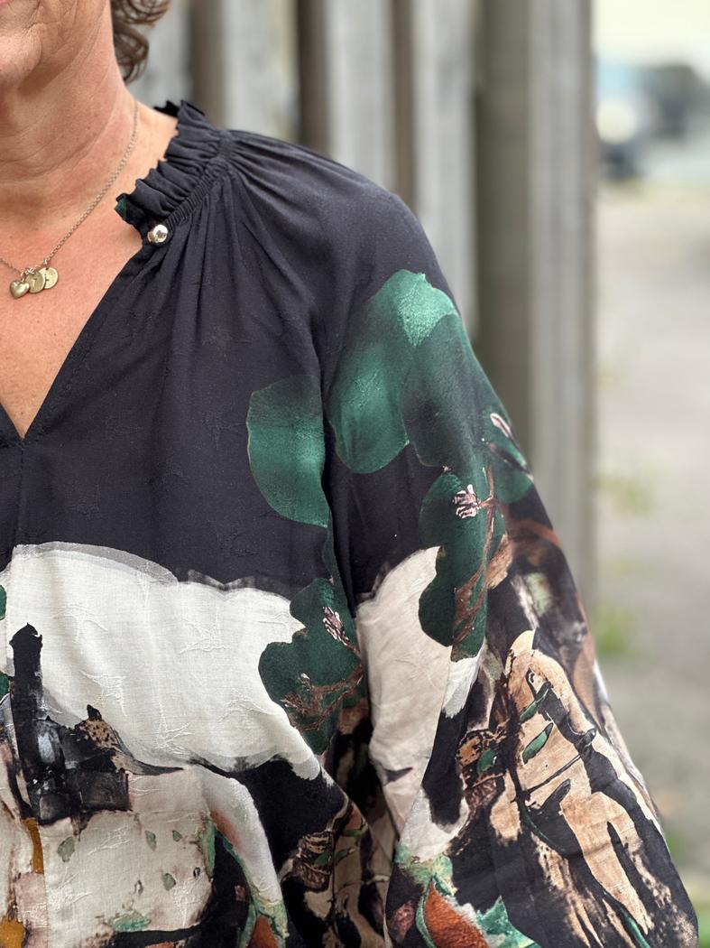 Bluse i viskose med abstrakt mønster i svart, grønt, hvitt og brunt, med rynket hals og knappdetaljer.