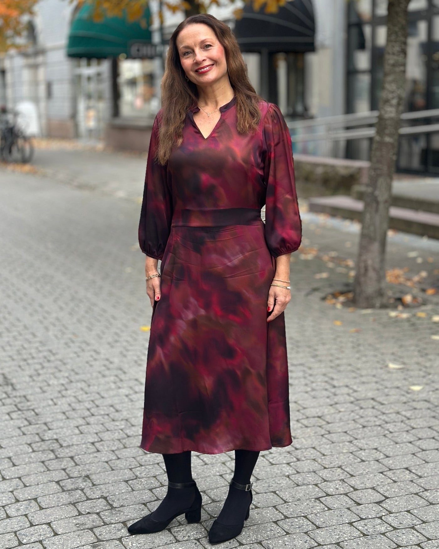 Kjole med røde og lilla nyanser, lange ermer og V-utringning.