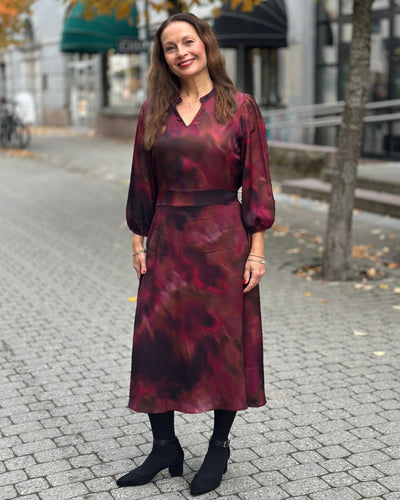 Kjole med røde og lilla nyanser, lange ermer og V-utringning.