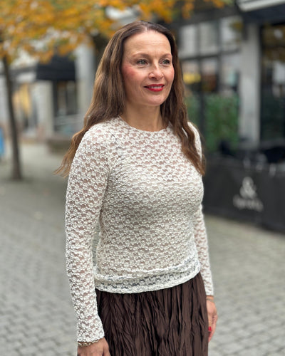 Person med tettsittende, langermet topp med blondeaktig mønster, utendørs med høstløv i bakgrunnen.