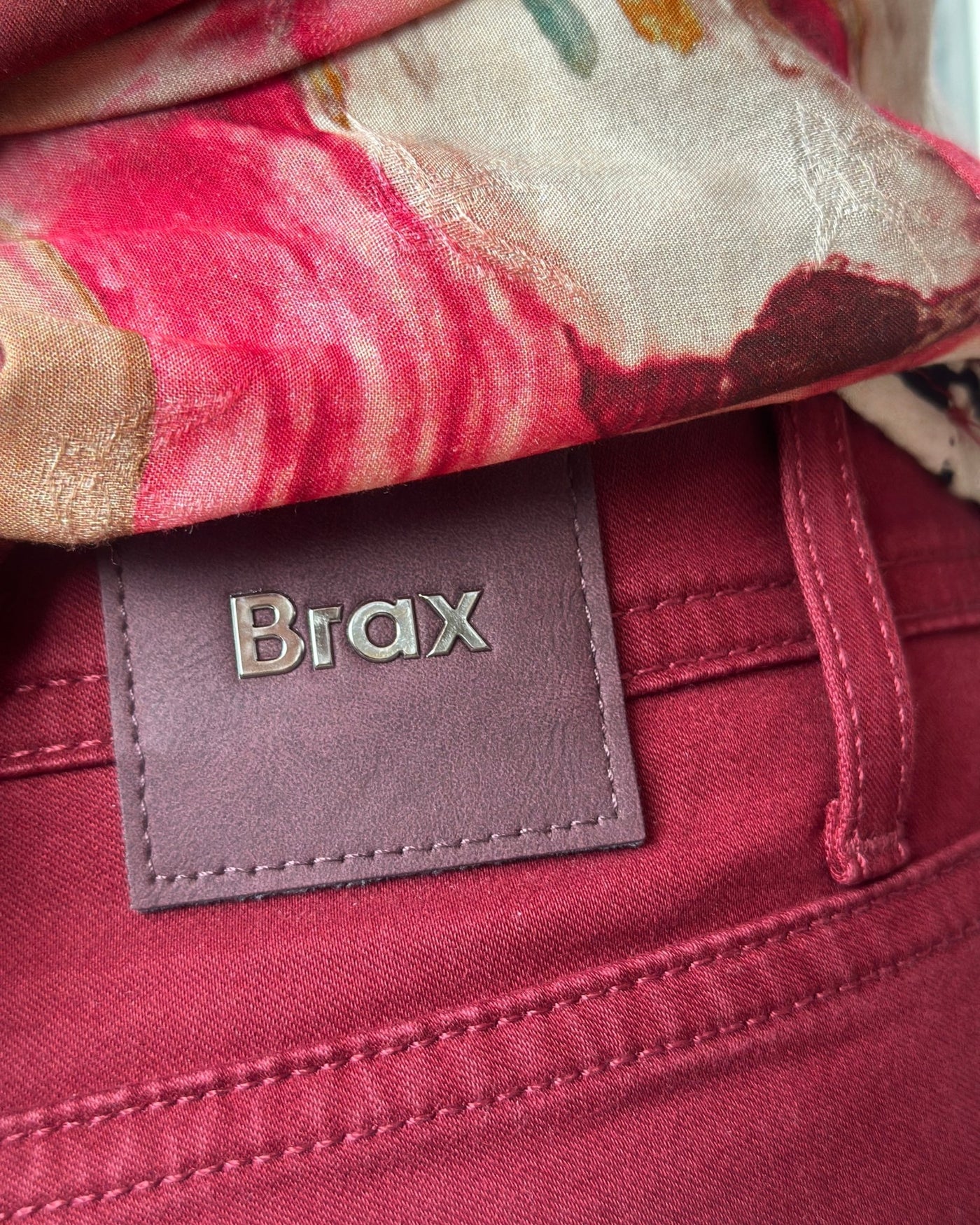 Dyp rød bukse med dekorative detaljer og et "Brax"-merke på baksiden.