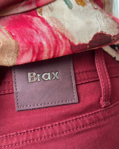 Dyp rød bukse med dekorative detaljer og et "Brax"-merke på baksiden.