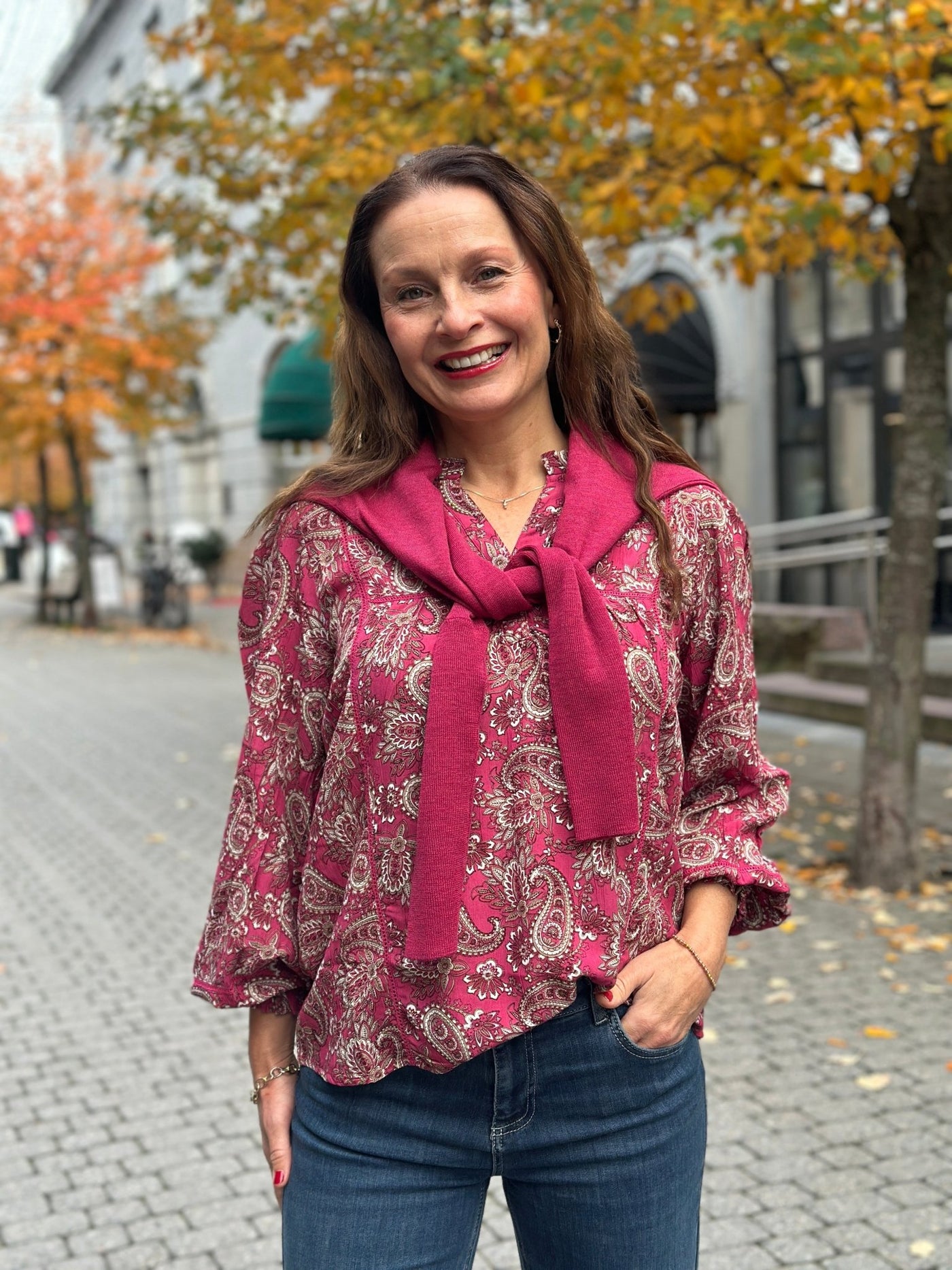 Kvinne i varm rosa paisleymønstret bluse med strikk på ermene, hvite og beige detaljer.