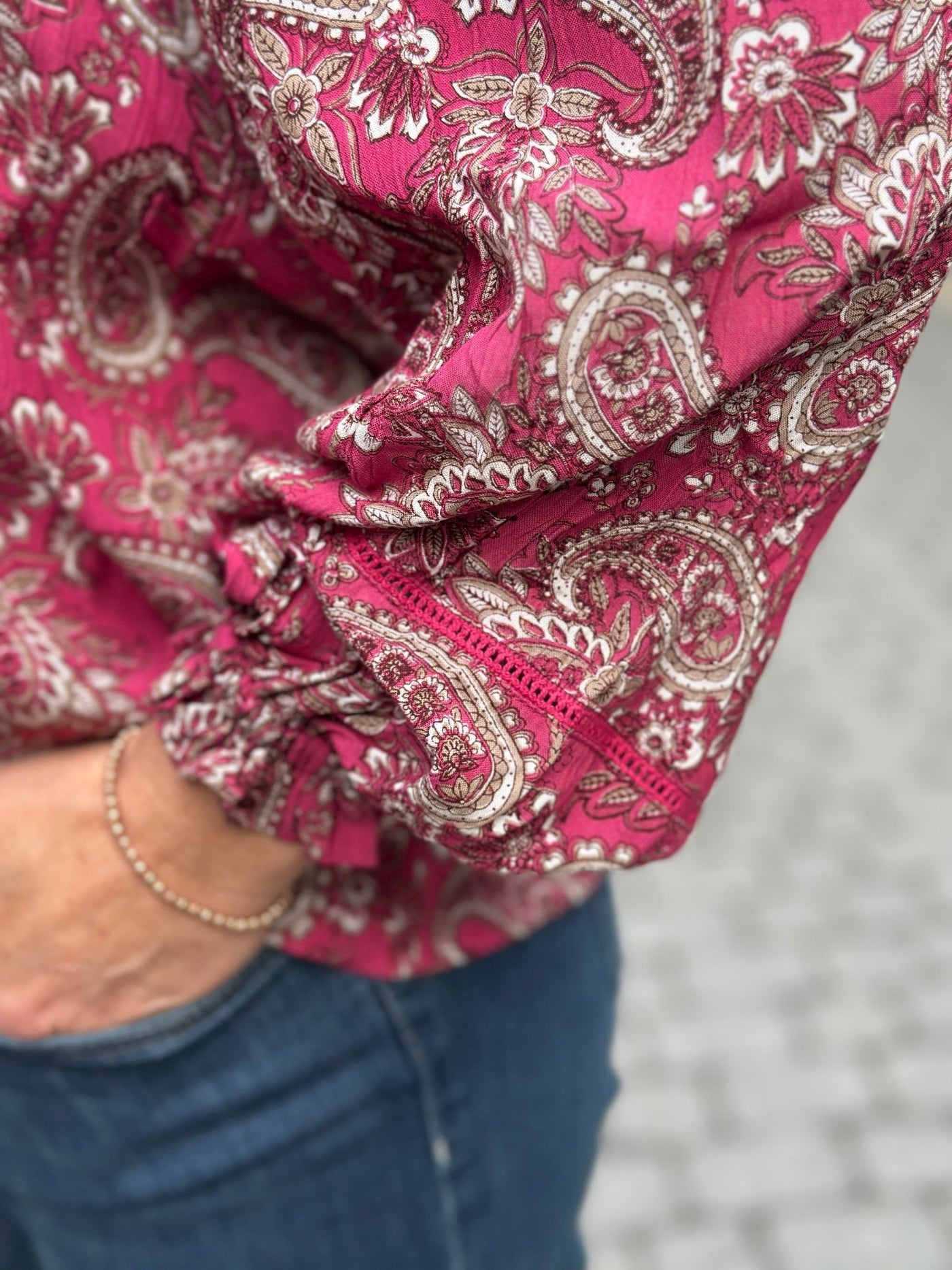 Nærbilde av en bluse med paisleymønster i rosa, hvitt og beige, med strikk på ermet.