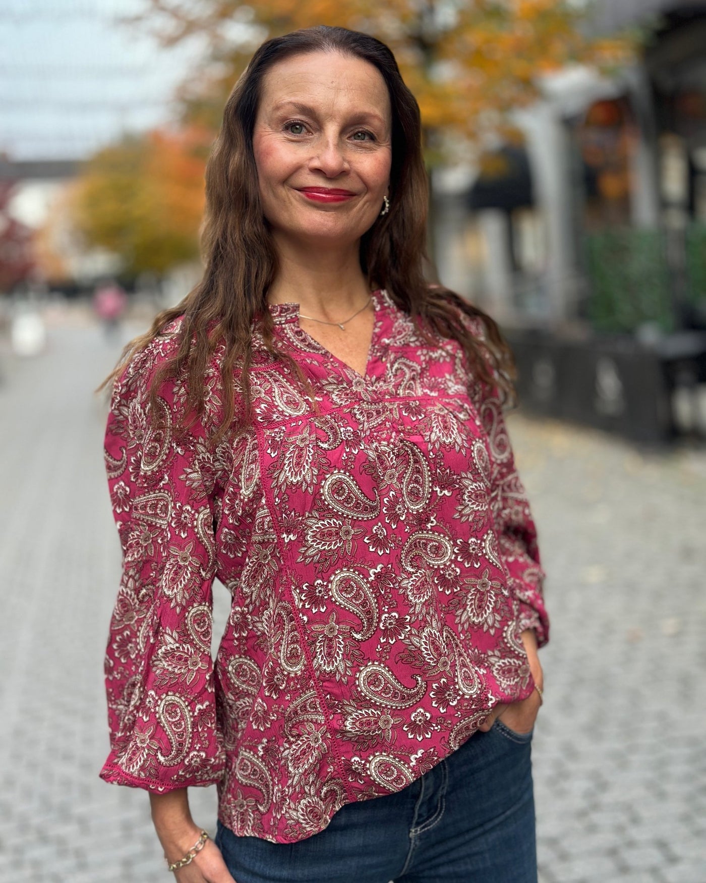 Kvinne med varm rosa paisleymønstret bluse, strikk på ermene, hvite og beige detaljer.
