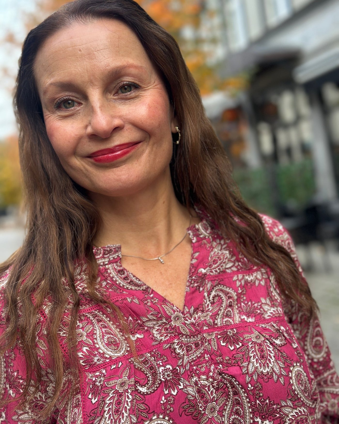 Kvinne i rosa paisleymønstret bluse med strikk på ermene, smilende med langt brunt hår.