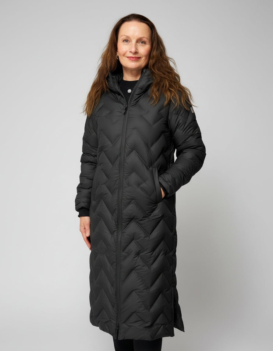 Lang, quiltet kåpe med boblemønster, hette og glidelås foran. Kvinne poserer iført kåpen.