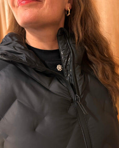 Nærbilde av sort, quiltet boblekåpe med hette og glidelås, delvis visning av ansikt og hår.