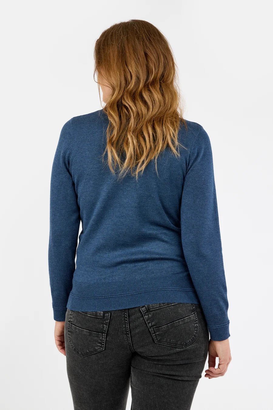 Blå genser med høy hals, ribbestrikket kant og lange ermer, sett bakfra, sammen med mørke jeans.