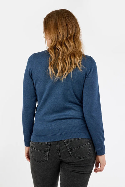 Blå genser med høy hals, ribbestrikket kant og lange ermer, sett bakfra, sammen med mørke jeans.