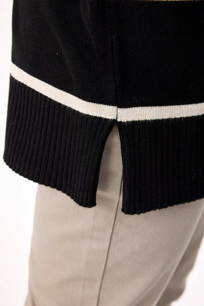 Nærbilde av genserens ribbestrikkede kant med splitt og kontraststripe, over lyse bukser.