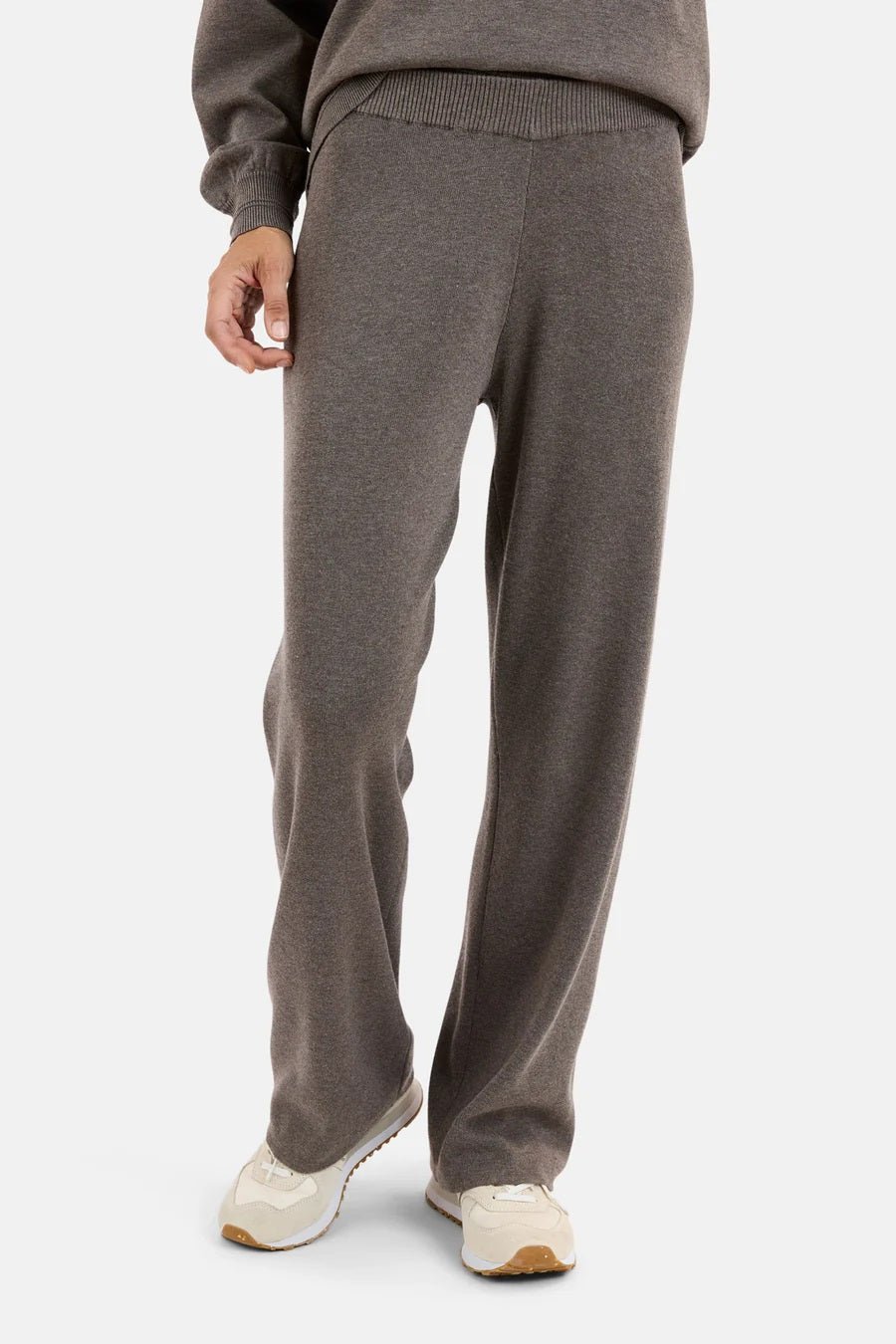 Grå bukse med elastisk linning, brede ben og løs passform, båret av en person med hvite joggesko.