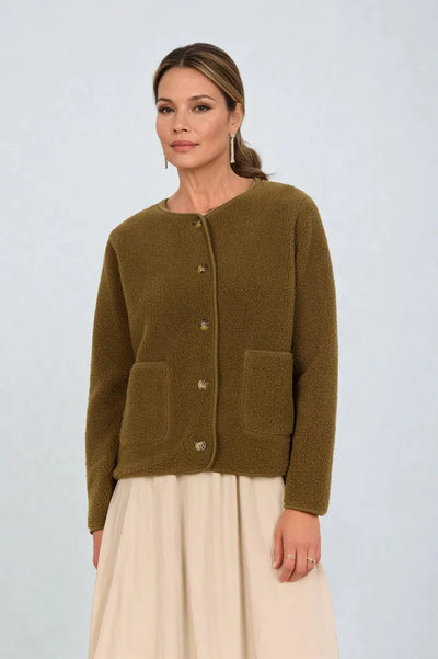 Person med olivengrønn cardigan med lommer og knapper, over en lys beige skjørt.