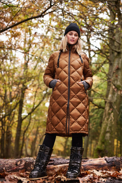 Lang brun dunkåpe med diamantmønster, glidelås og lommer, i skogkledd landskap.
