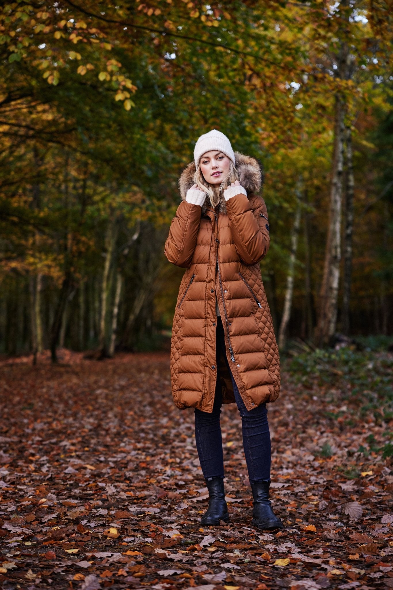 Lang brun dunkåpe med pelskant på hetten, person står i en skog med høstløv på bakken.