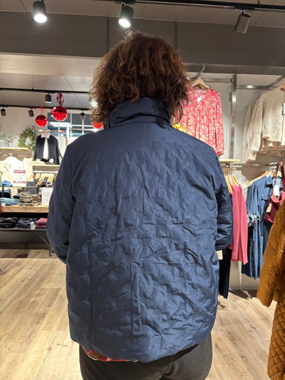 Person med blå jakke med mønster, sett bakfra i butikk med tregulv og klær på stativ.