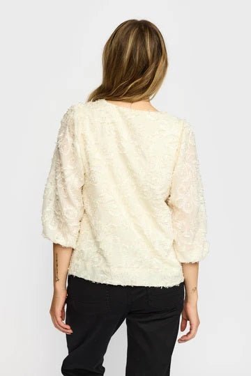 Kvinne med hvit, teksturert Mira Bluse med trekvart ermer og rund hals, sett bakfra.