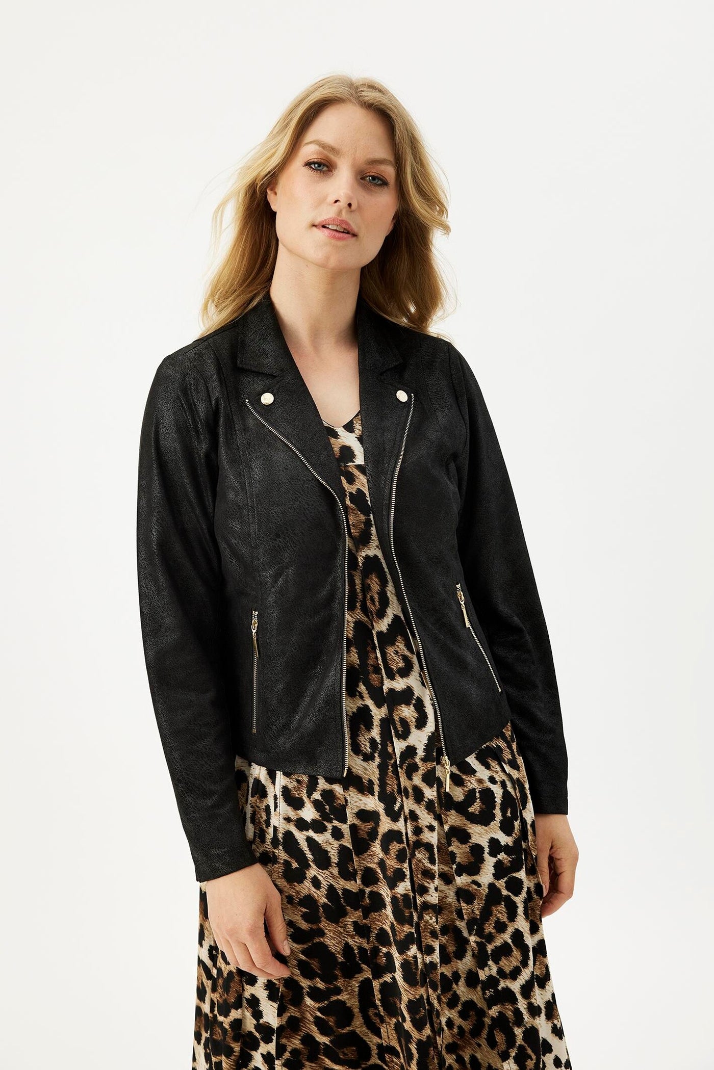 Svart jakke med glidelås og krage med trykknapper, brukt over en leopardmønstret kjole.