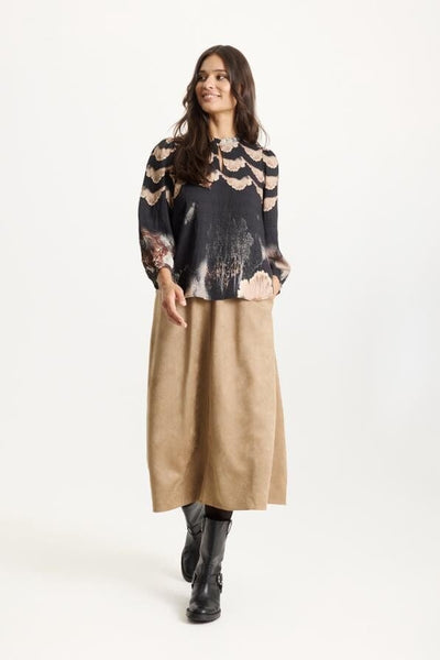 Bluse med bølgete mønster, lange ermer, løs passform. Beige skjørt, svarte støvler.