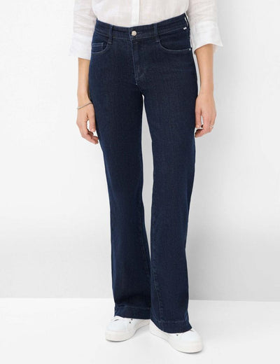 Mørkeblå jeans med høy midje og sleng, hvit skjorte og hvite joggesko.