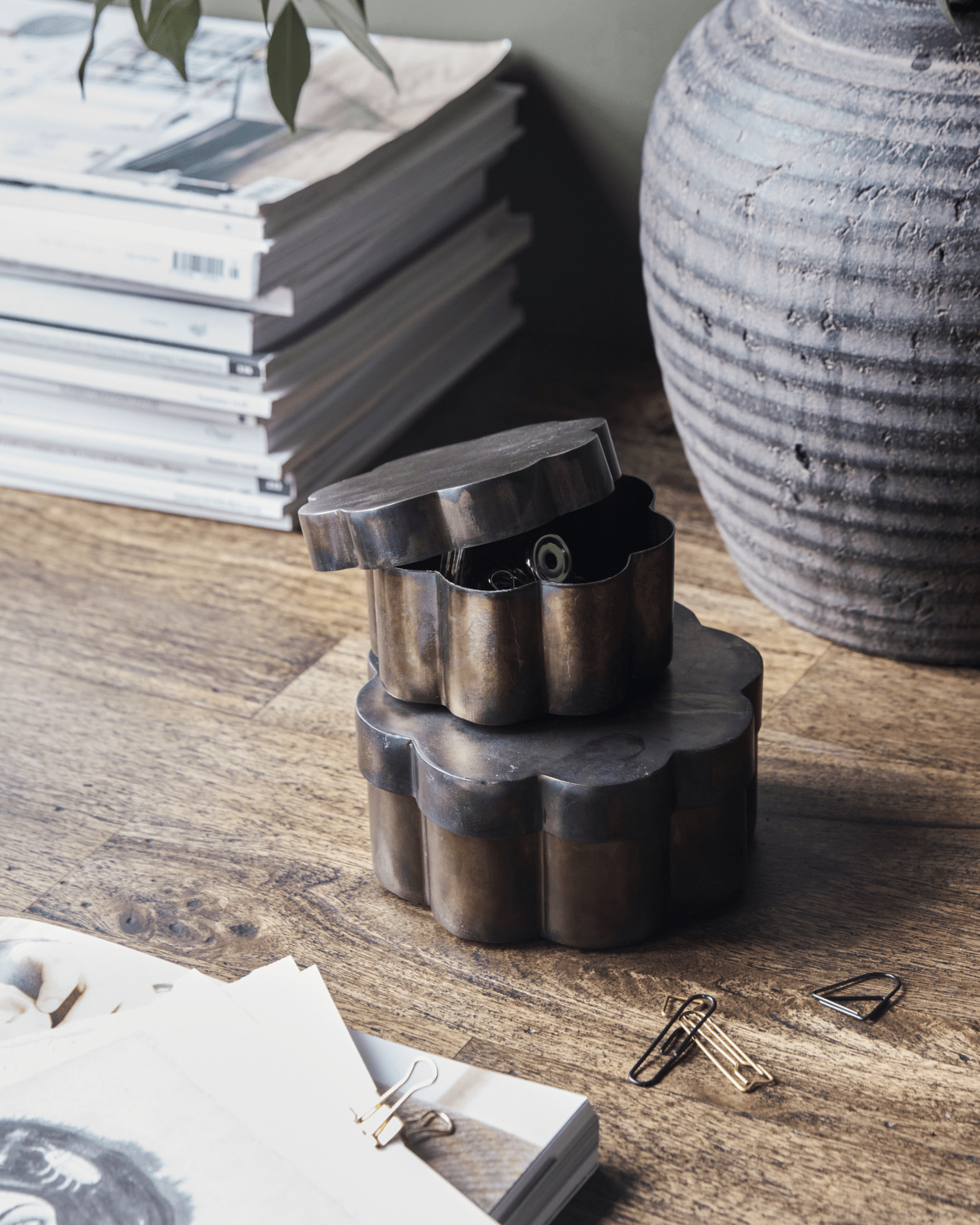 To beholdere med lokk i antikk brun, bølget design, står stablet på et bord med papirklips.