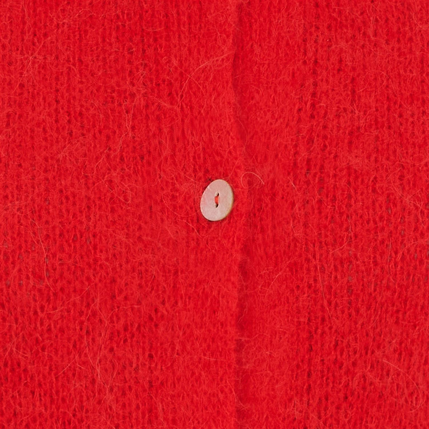 Nærbilde av rød strikkejakke med en knapp, som viser teksturen og fargen på stoffet.