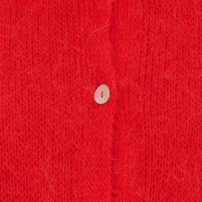 Nærbilde av rød strikkejakke med en knapp, som viser teksturen og fargen på stoffet.