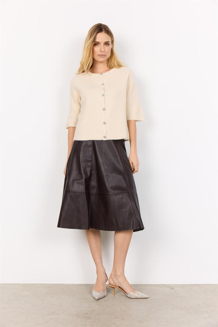 Beige cardigan med knapper, trekvart ermer og strikket tekstur. Kombinert med mørkt skjørt.
