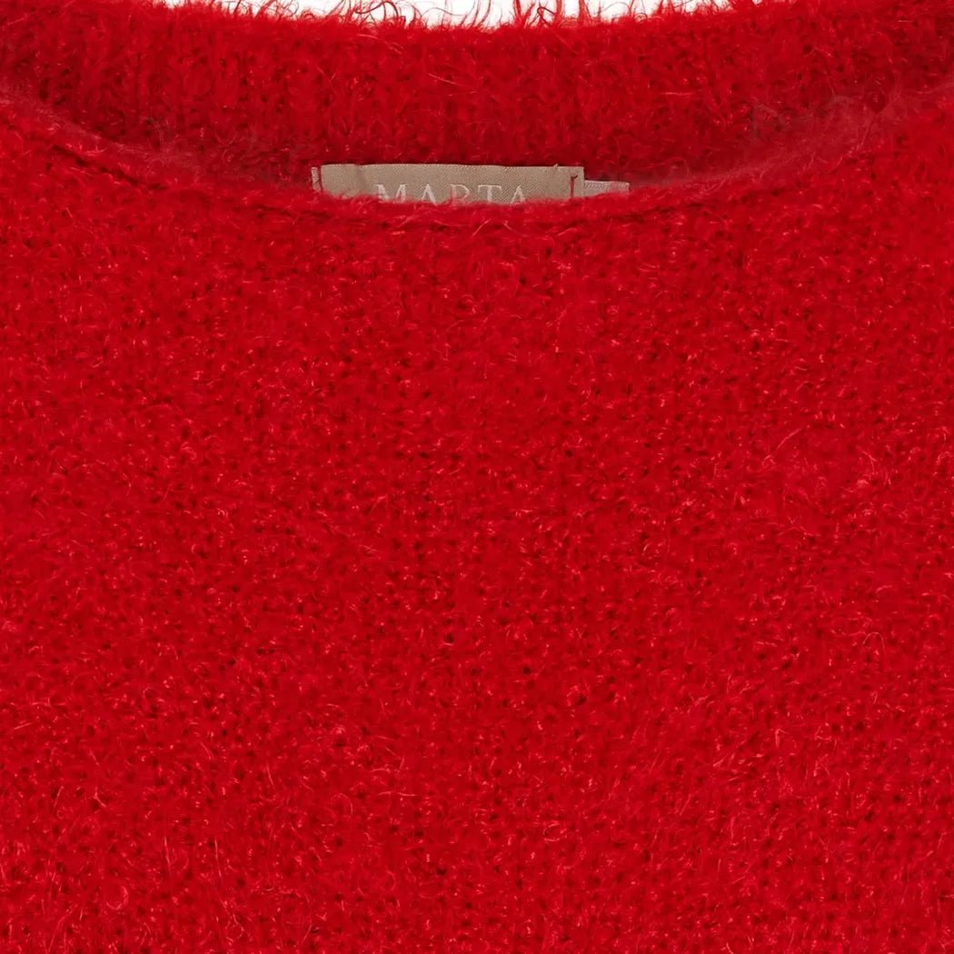 Rød, myk og lodden strikket tekstur med rund halslinje, etikett delvis synlig øverst.